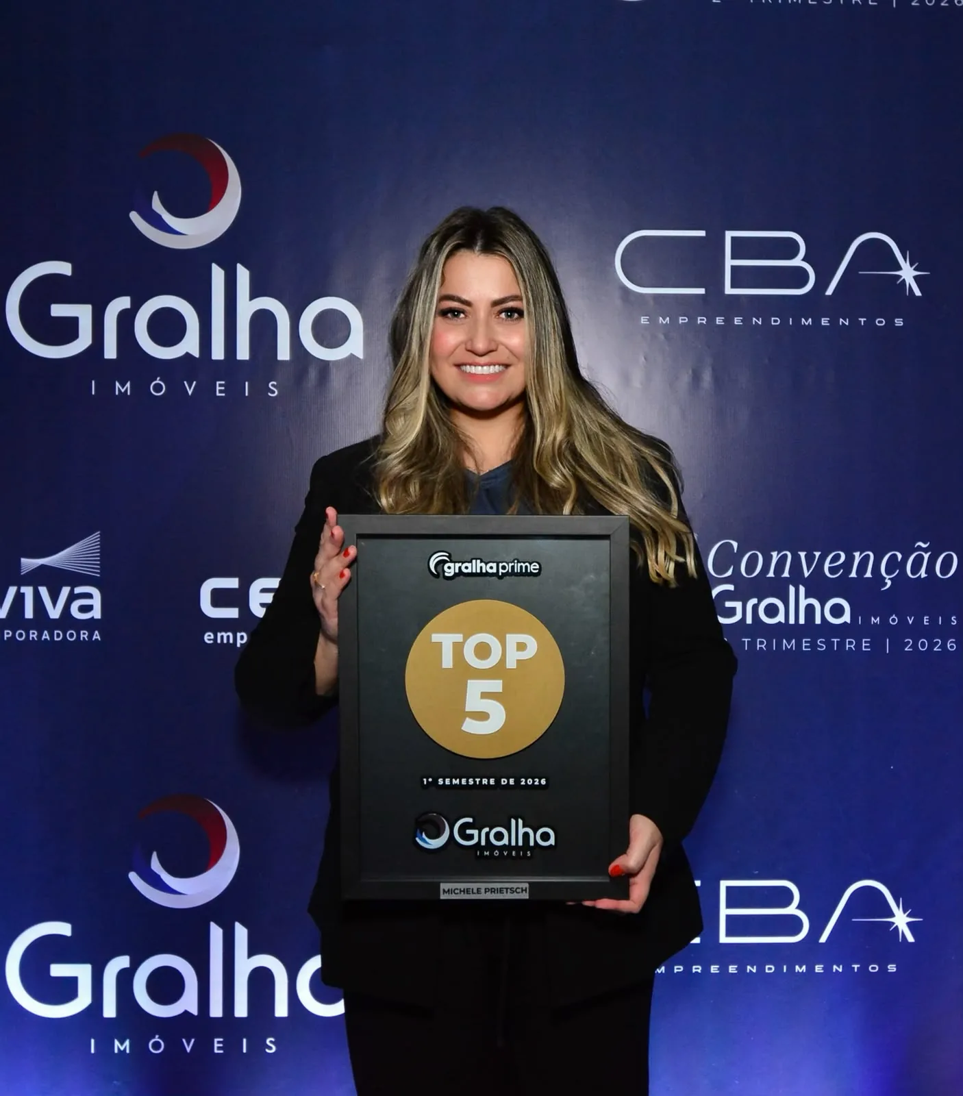 Michele Prietsch segura a placa Gralha Prime Top 5 do primeiro semestre de 2026 na convenção da Gralha Imóveis